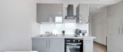 A modern kitchen with grey cabinetry, a built-in oven, and a stainless steel range hood.