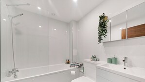 A modern bathroom with a glass-enclosed shower, a white toilet, and a vanity with a mirror. - Hotel Studio Apartment in East London (Ilford)