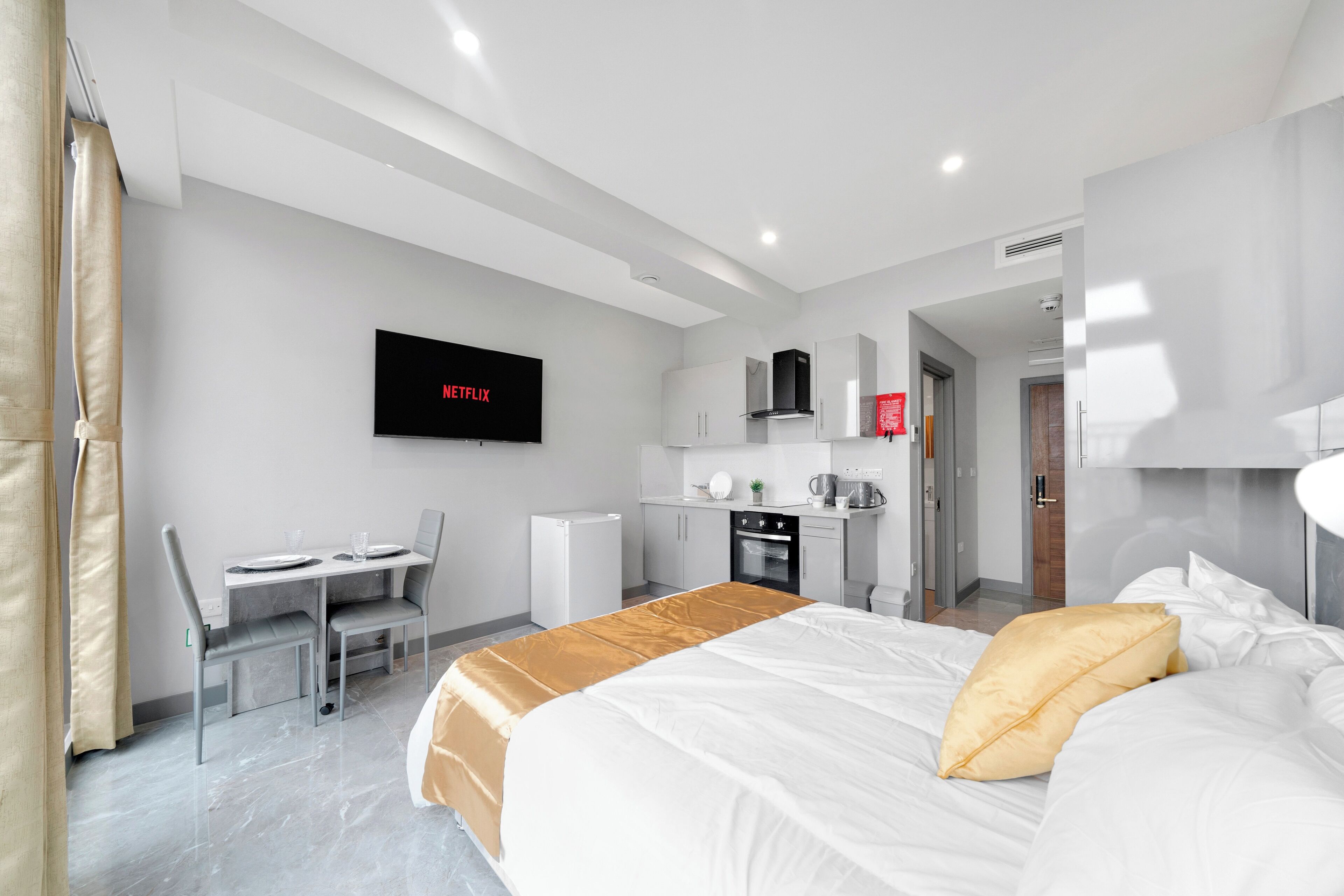 Ein modernes Hotelzimmer mit Bett, Schreibtisch, Küchenzeile und einem Fernseher, der 'NETFLIX' anzeigt.