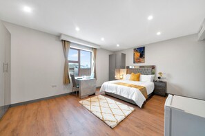 A modern bedroom with a bed, desk, and a view of the city.