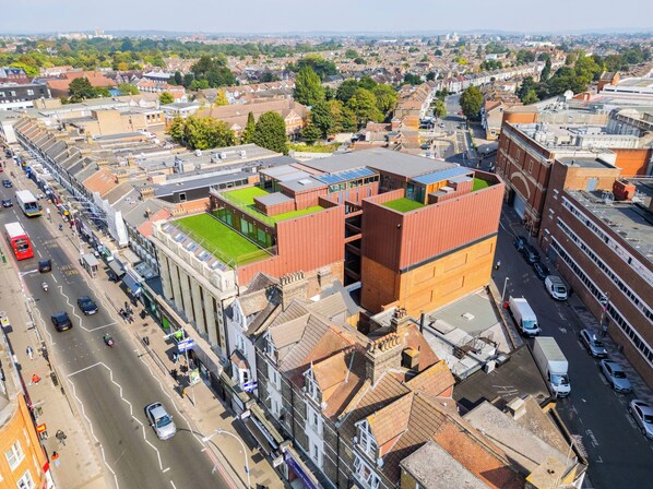 A modern building with a green rooftop garden, a parking area, and a street view with cars and pedestrians.