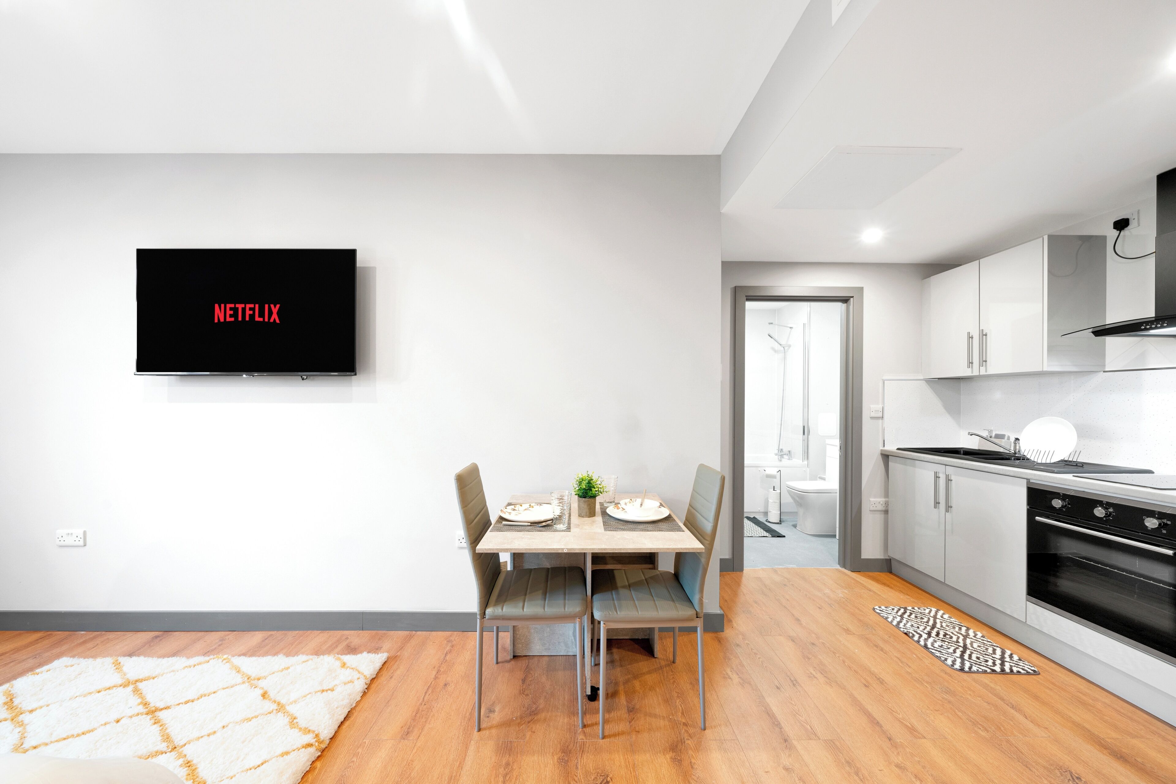 A modern kitchen with white cabinets, a black oven, and a dining area with a table and chairs.