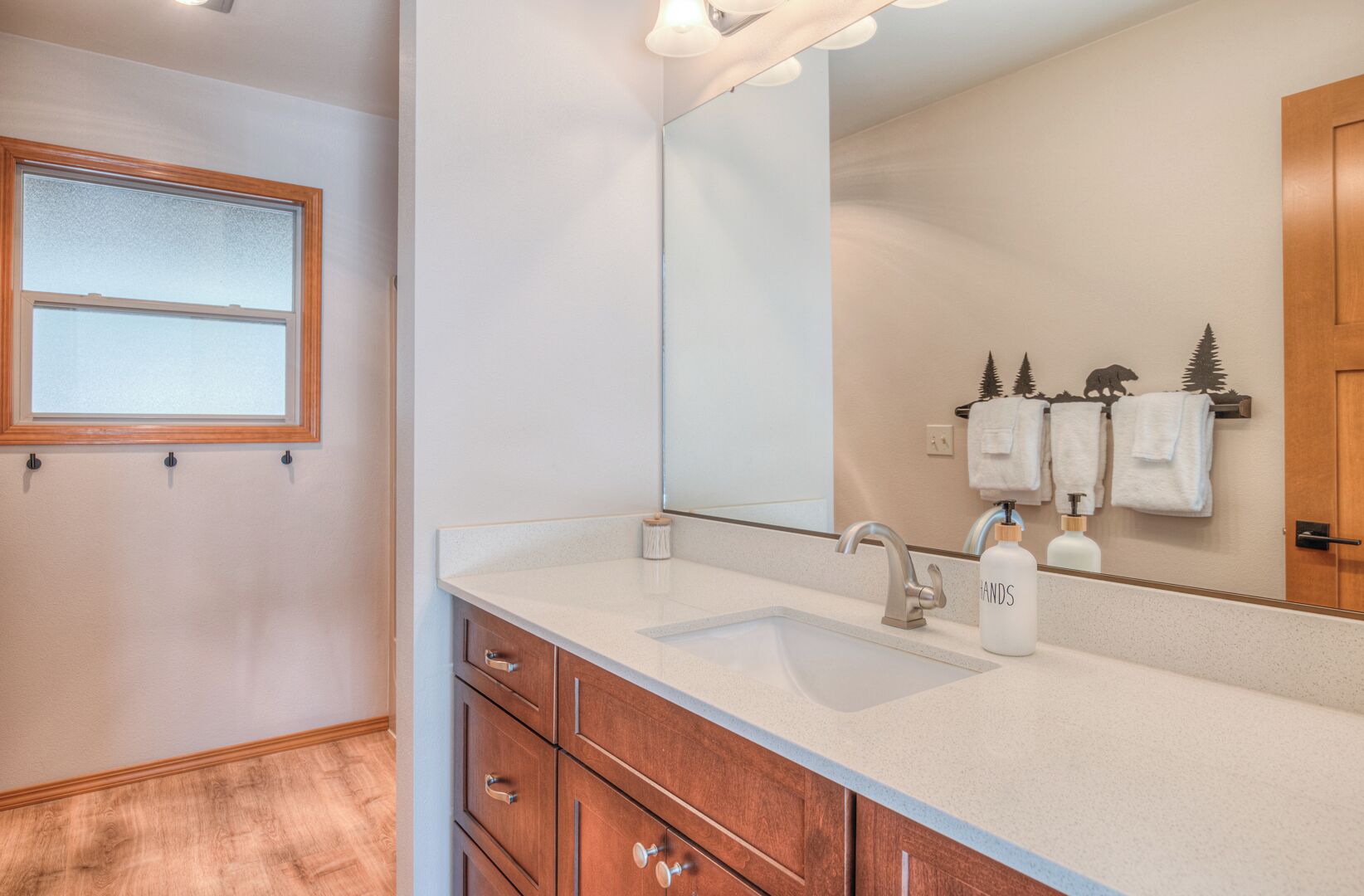 A bathroom with a white sink, wooden cabinets, a large mirror, and a window with frosted glass.