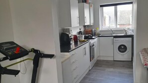 A compact kitchen with a washing machine, a treadmill, and a window providing natural light.