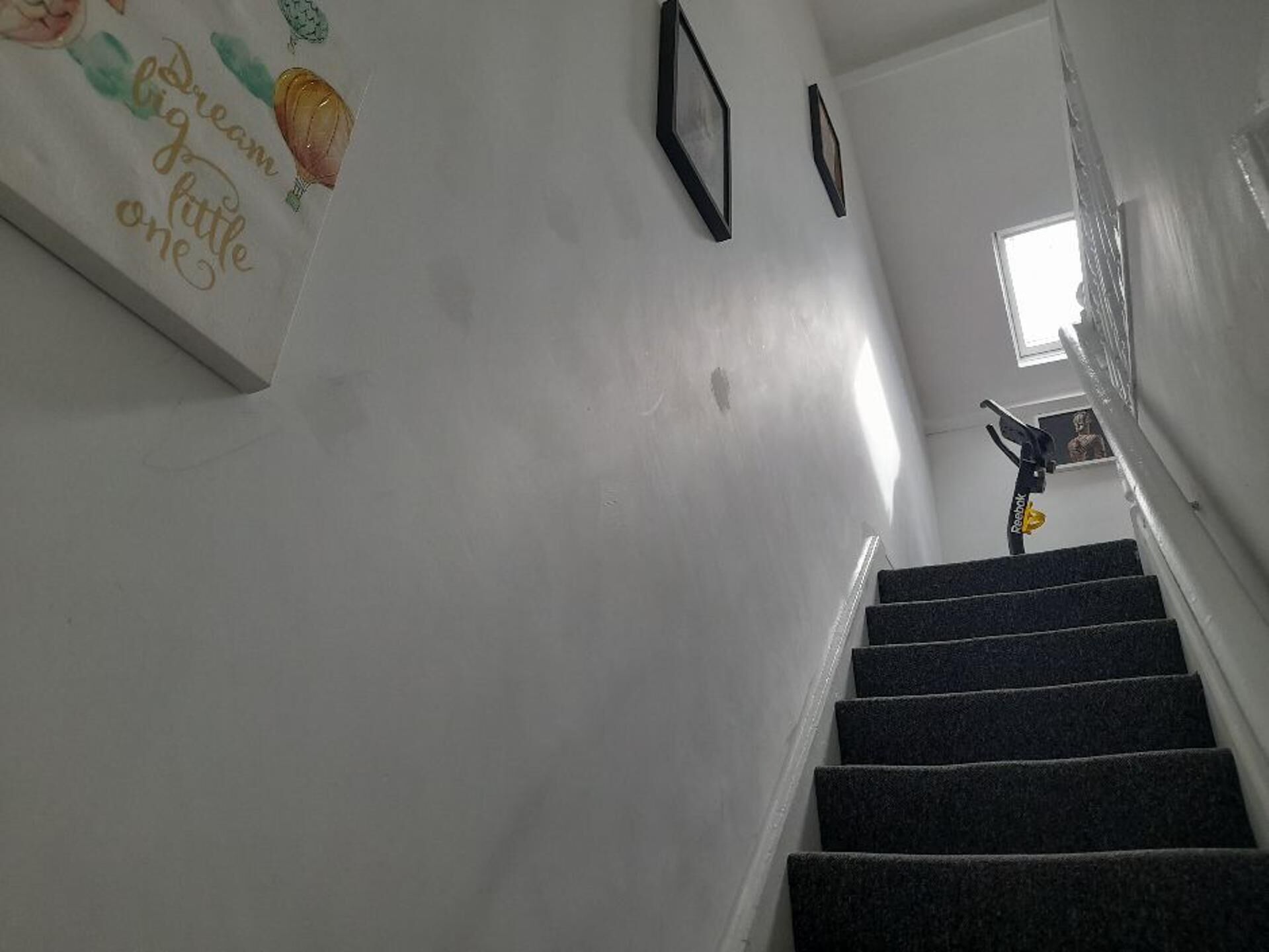 Una escalera con barandilla, una pared con cuadros enmarcados y un ventanal en la parte superior.