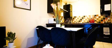 A compact kitchen with a dining area, featuring a tiled backsplash, modern appliances, and a dining table with chairs.
