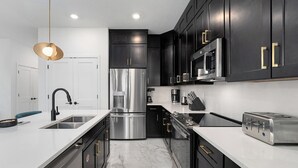 A modern kitchen with black cabinets, stainless steel appliances, and a white countertop. - Villa Celestia | Posh Home w/ Grand LR/DR, Dollhouse BR & Pool - Near Waterparks (Orlando)