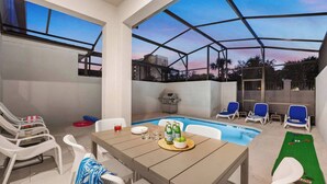 Un espace extérieur abrité comprenant une piscine, des chaises longues et une table dressée pour les repas.