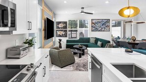 A modern kitchen with a built-in oven, a microwave, and a toaster. There is a dining area with a green sofa and a coffee table.
