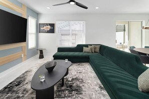 Un salon moderne avec un canapé d’angle, une table basse, un téléviseur à écran plat et un ventilateur de plafond.