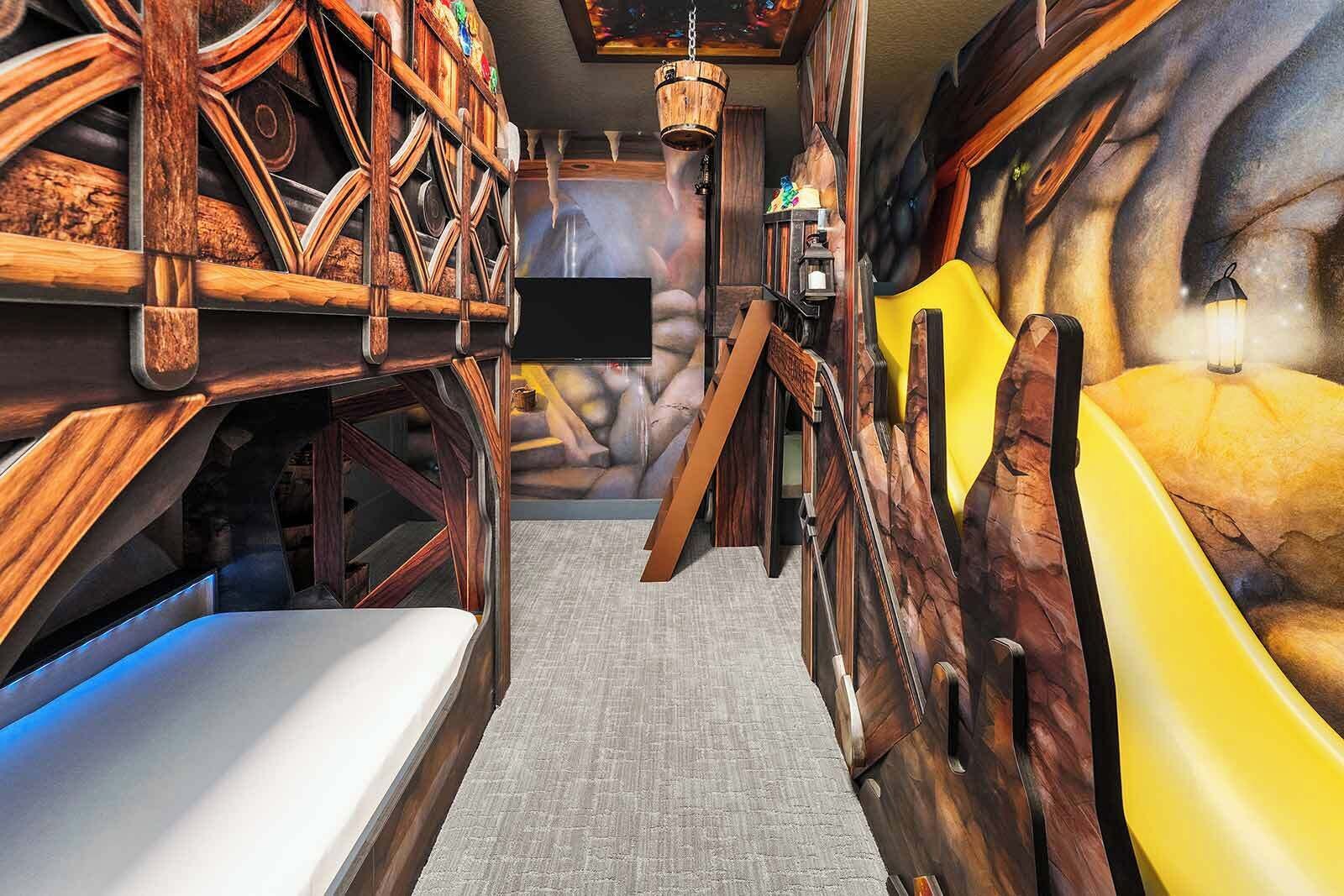 A room with a wooden bunk bed, a yellow slide, and a TV mounted on the wall.