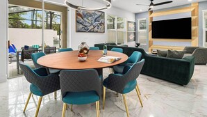 Una sala moderna con una mesa redonda de madera, sillas color turquesa, un sofá verde y un televisor de pantalla plana.