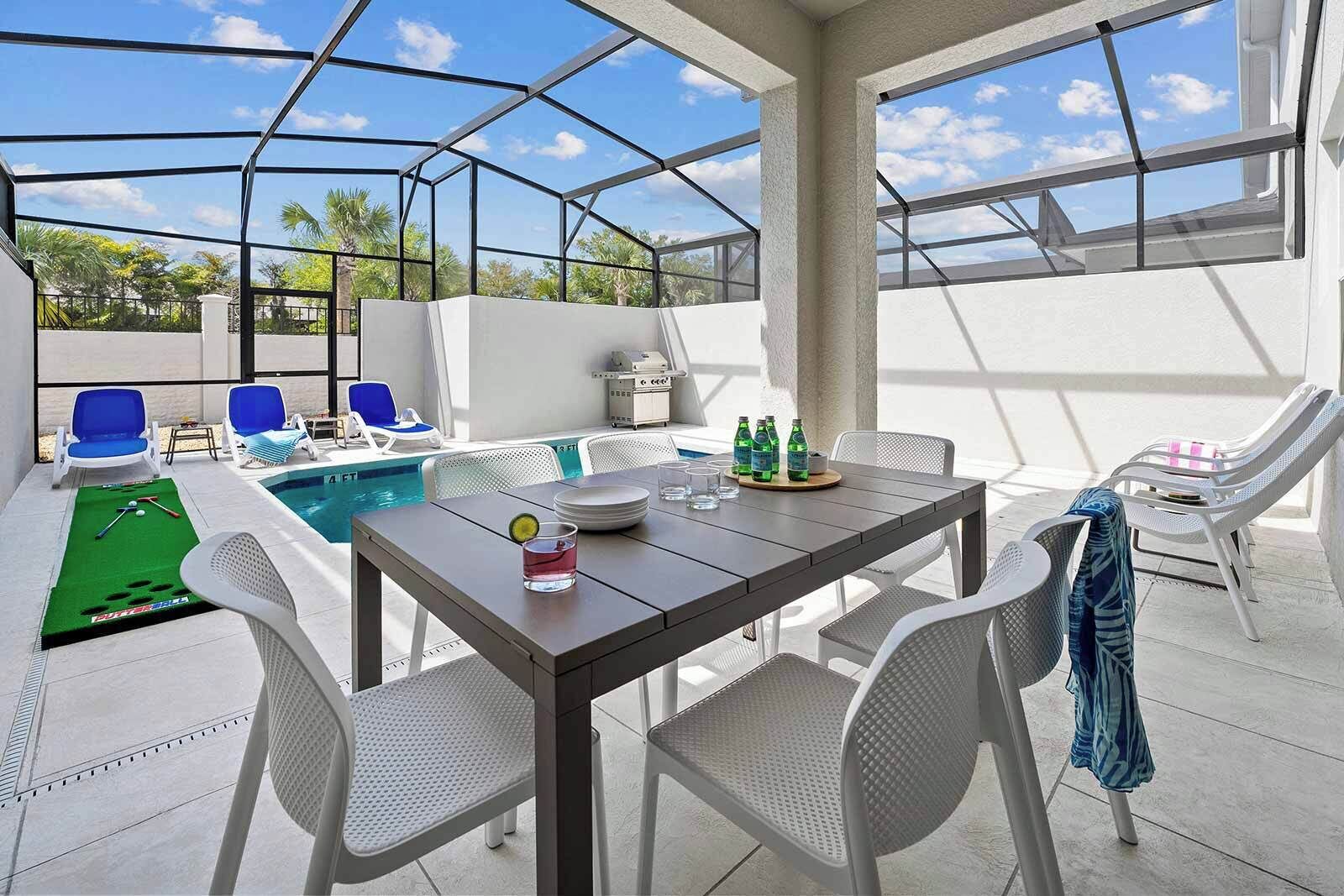 A covered outdoor area with a pool, lounge chairs, and a dining table.