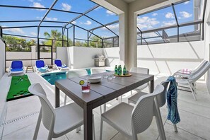 A covered outdoor area with a pool, lounge chairs, a table with drinks, and a table tennis table. - Toby's Treehouse | Cozy NEW I-Drive Home w/ Grand LR/DR, Full Kitchen & PVT Pool (Orlando)
