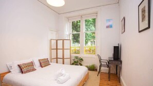 A bedroom with a bed, a desk, a chair, and a window with a view of trees.