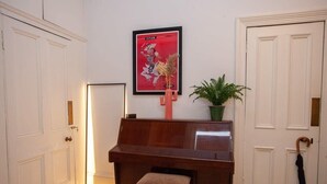 A room with a piano, a framed picture on the wall, a potted plant, and a door with an umbrella.