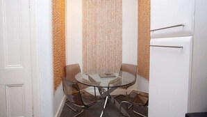 A small, modern room with a glass table and four chairs, a white door, and a textured wall panel.