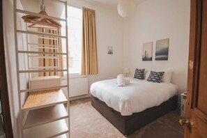 A bedroom with a bed, a wooden shelf unit, a radiator, a window with curtains, and two wall-mounted pictures. - Stylish West End Apartment in Glasgow (Glasgow City)