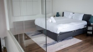 Um quarto moderno com uma cama grande, uma mesa de cabeceira e uma parede divisória de vidro.
