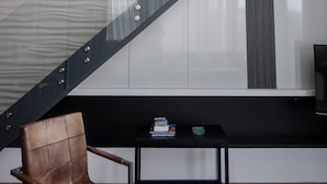 Um interior moderno com escada de vidro, uma poltrona de couro e uma pequena mesa com livros.