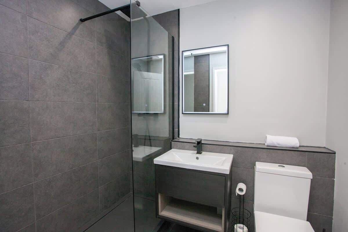 A modern bathroom with a glass shower enclosure, a white sink, a mirror, and a toilet.