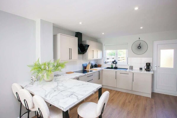 A modern kitchen with a marble countertop, white cabinetry, and a dining area with a white table and chairs.