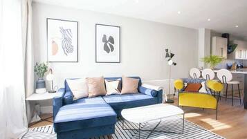 A modern living room with a blue sofa, a yellow chair, and a kitchen area in the background.