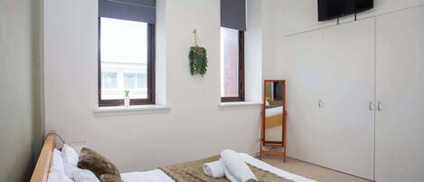 Une chambre à coucher avec un lit, une armoire, un téléviseur et une fenêtre agrémentée d’une plante.