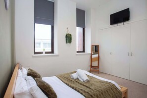 A bedroom with a bed, a wardrobe, a television, and a window with a plant.