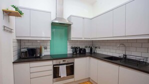 A modern kitchen with white cabinets, a stainless steel range hood, a built-in oven, a microwave, and a sink with a dish rack. - Stunning City Centre Duplex (Glasgow City)