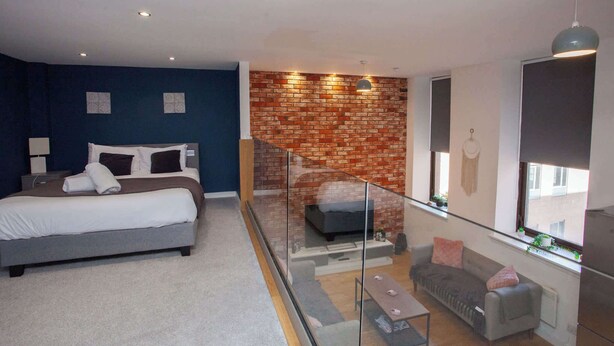 A modern bedroom with a bed, a glass-walled fireplace, a sofa, and a dining area. - Stunning City Centre Duplex (Glasgow City)