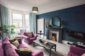 Ein Wohnzimmer mit Kamin, Fernseher und violetten Sofas.