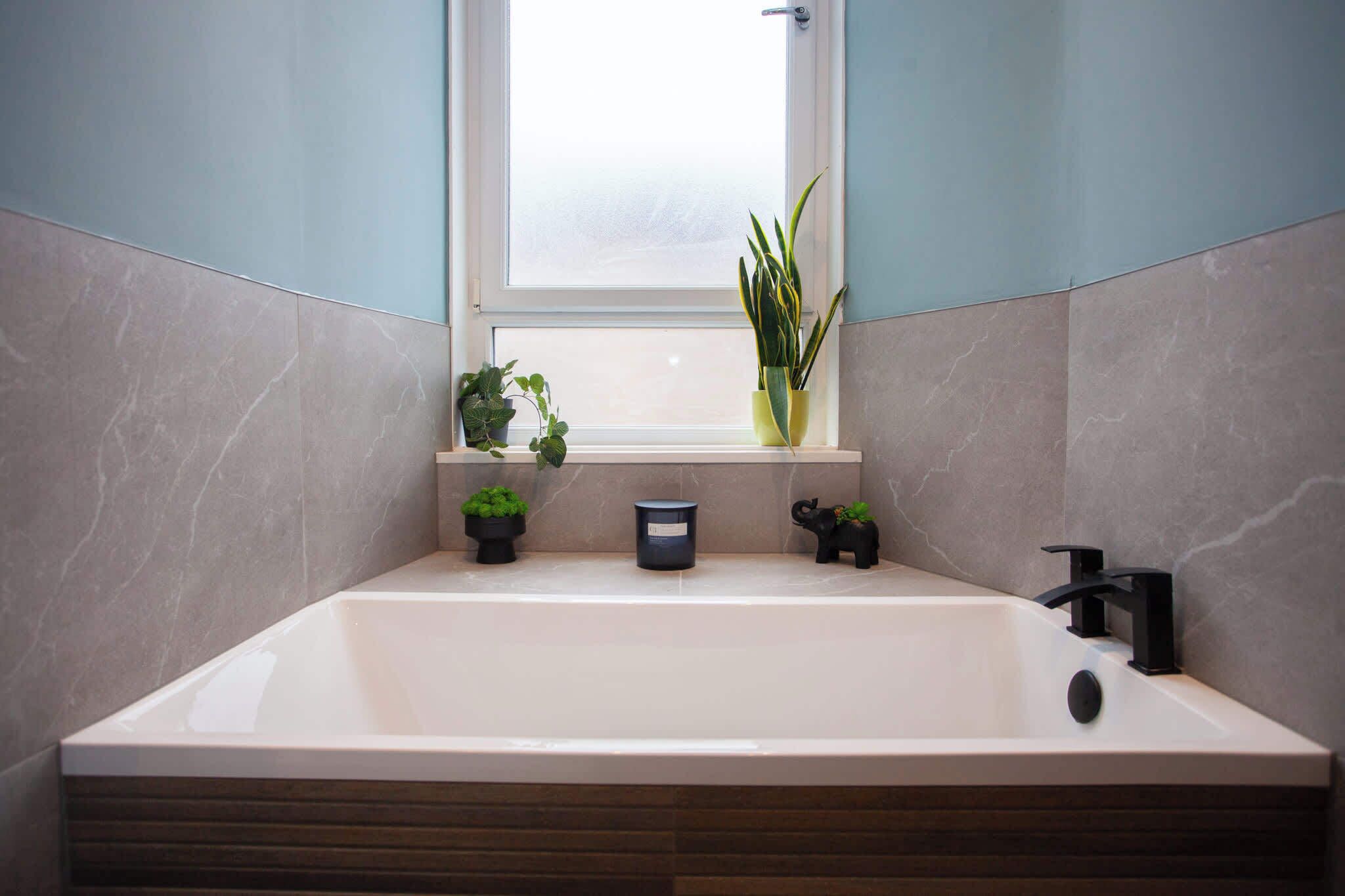 A modern bathroom with a bathtub, a window, and potted plants.