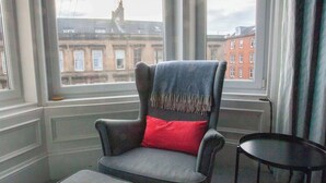 Una habitación con un sillón gris con un cojín rojo, un reposapiés a juego y una pequeña mesa negra.