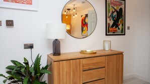 A modern room with a wooden cabinet, a round mirror, a lamp, and a framed Spider-Man poster. - West End Flat with Private Terrace Glasgow (Glasgow City)
