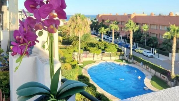 A balcony with a view of a swimming pool, surrounded by palm trees and a clear sky.