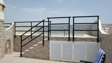 Un área de piscina en la azotea con un muro de piedra, una escalera de piscina y una silla de descanso con cojín a rayas.