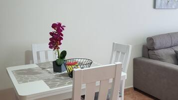 Un coin repas avec une table et des chaises blanches, un vase rempli de fleurs violettes et un tableau accroché au mur.