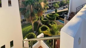 A modern building with a balcony overlooking a landscaped area with palm trees and a swimming pool.