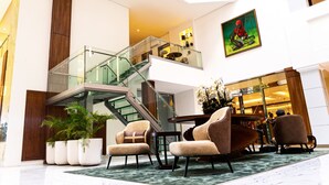 A modern lobby with a glass staircase, comfortable seating, and a large potted plant. - Summit Hotel and Apartments VGC (Lekki)