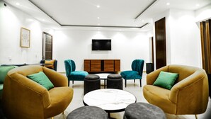 A modern living room with two yellow armchairs, a round coffee table, and a TV mounted on the wall. - Summit Hotel and Apartments VGC (Lekki)