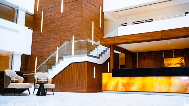 A modern lobby with a wooden wall, a glass staircase, and a reception desk with a marble-like surface. - Summit Hotel and Apartments VGC (Lekki)