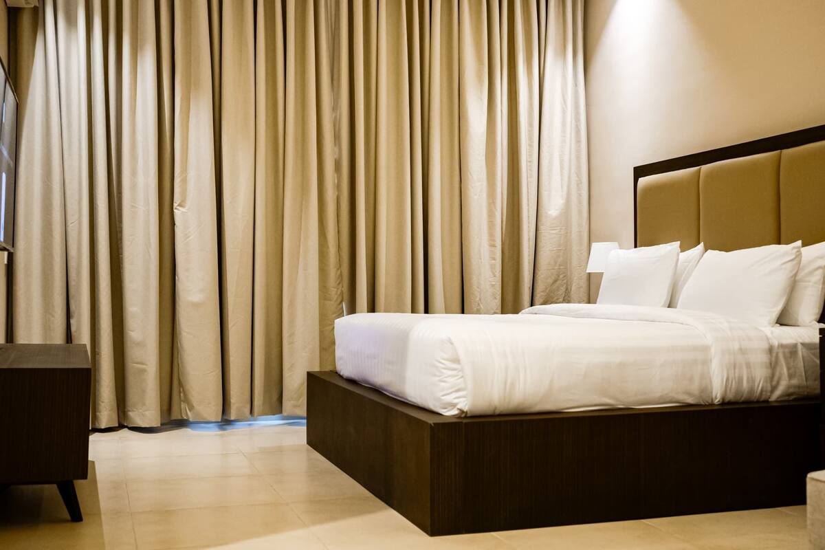 A hotel room with a bed, bedside table, and a TV mounted on the wall.