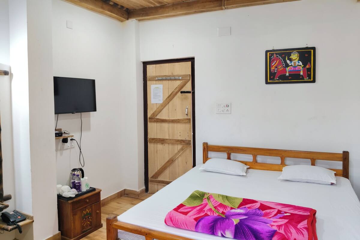 Un dormitorio con una cama de madera, un televisor montado en la pared, un armario de madera y una puerta con marco de madera.