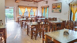 A restaurant with wooden tables and chairs, a ceiling fan, and a painting on the wall. - Khoai Village Resort (Bolpur)