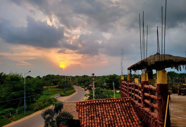 A rural road leading to a thatched-roof structure with a tiled roof.