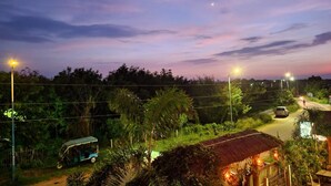 A rural road at dusk with a thatched-roof house, a tuk-tuk, and streetlights. - Khoai Village Resort (Bolpur)