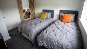 Un dormitorio con dos camas, cada una con cabecero, ropa de cama gris y un espejo en la pared.