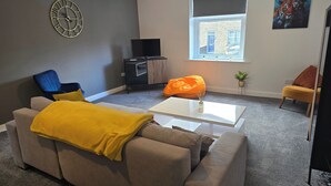 Una sala de estar con un sofá, una mesa de centro, un televisor y un ventanal con vistas a un edificio.