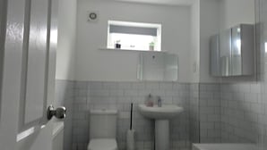 Un baño con azulejos blancos, ventana, lavabo e inodoro.